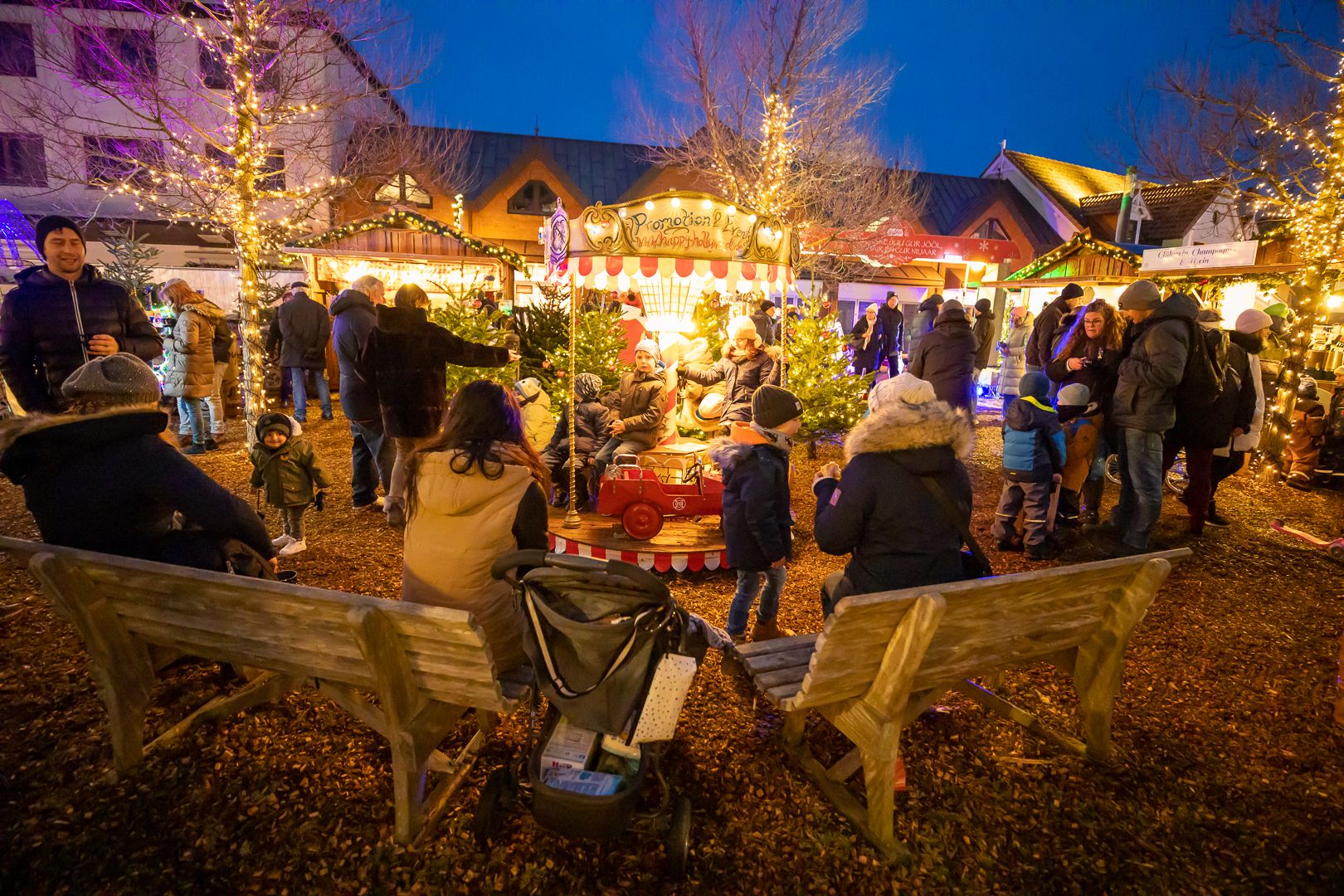 Besucher des Sylter Wintermarktes sitzen auf Bänken und schauen dem Treiben auf dem geschmückten Markt zu