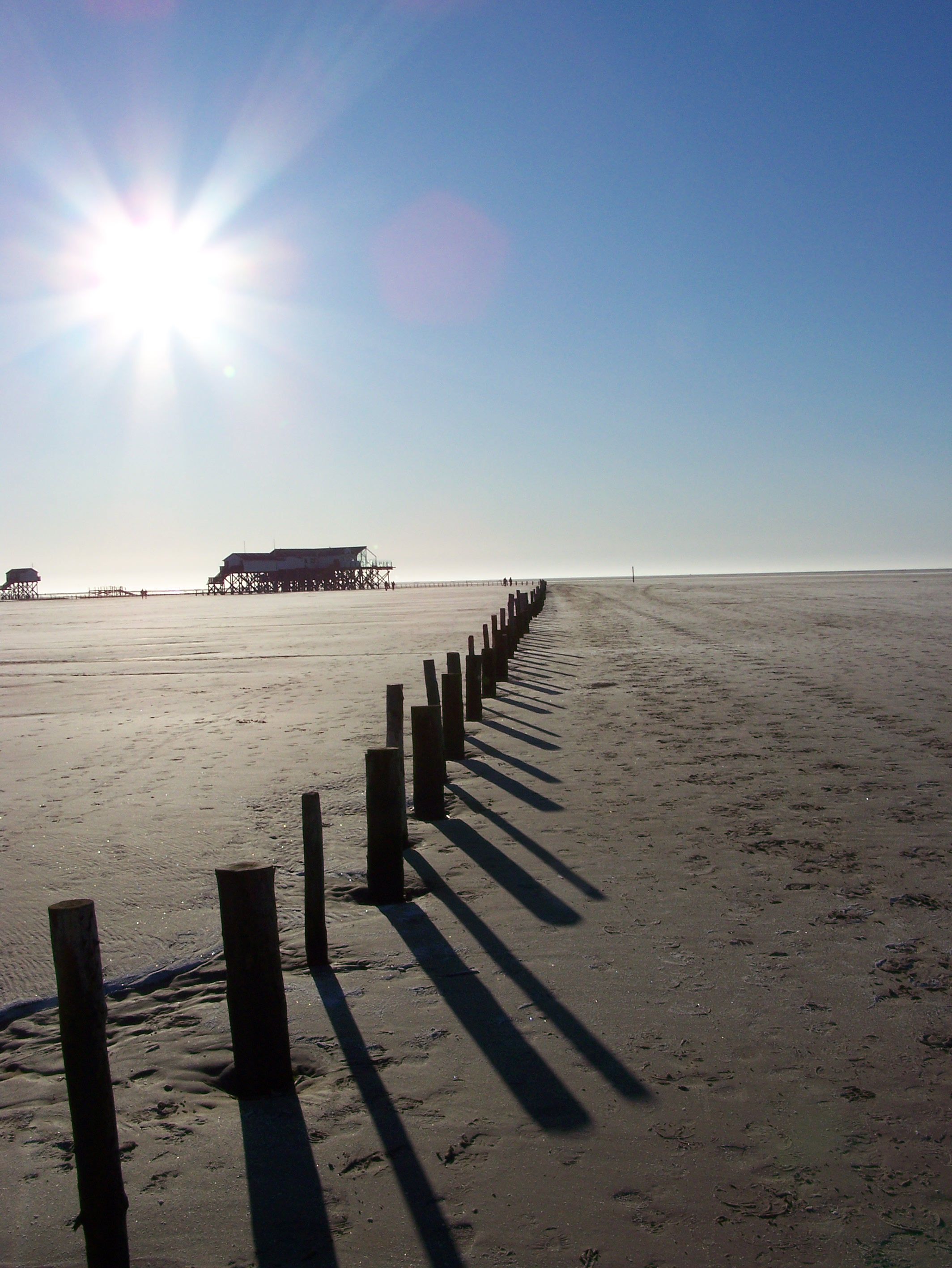 Blick über den weiten Sandstrand von St. Peter-Ording hin zu einer Pfahlbaute im Hintergrund