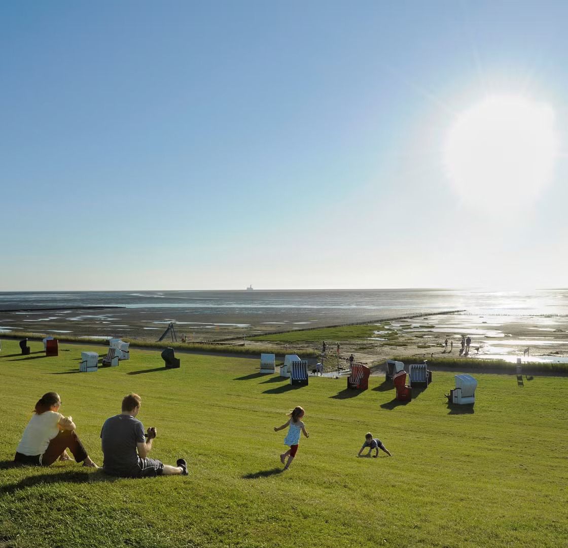 Familie sitzt am Deich der Friedrichskoog-Spitze und blickt auf das Watt hinaus