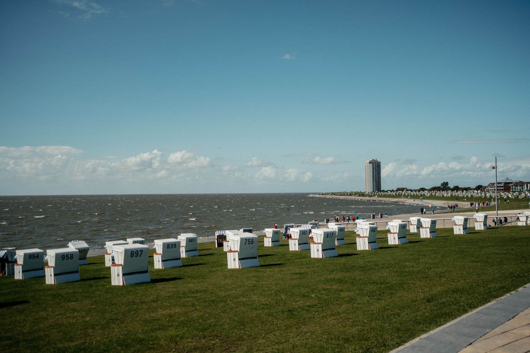 Viele Strandkörbe stehen auf dem grünen Deich an der Haupttribüne des Büsumer Strandes, im Hintergrund steht das Hochhaus von Büsum