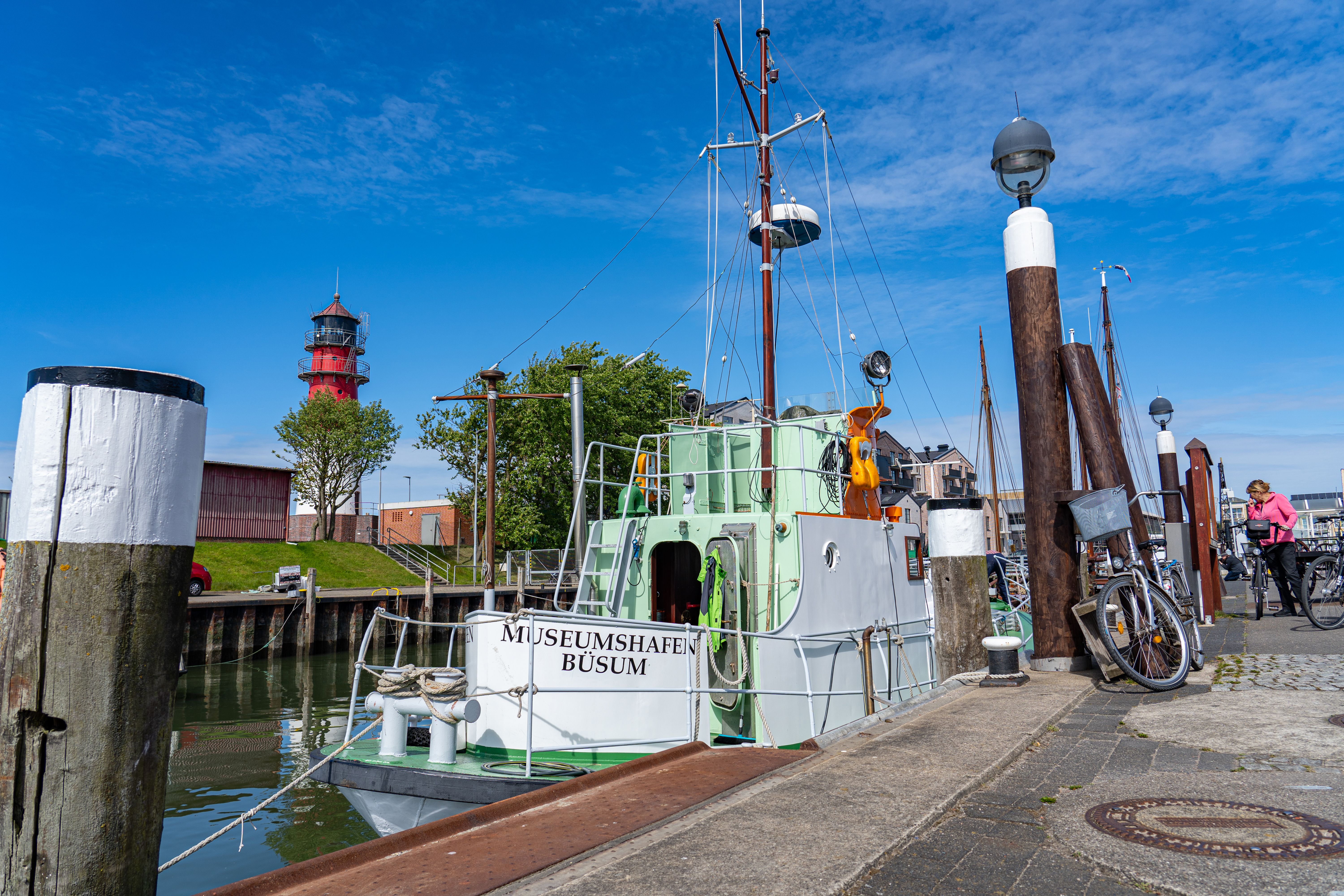 Ein Schiff steht im alten Museumshafen von Büsum, im Hintergrund steht der Büsumer Leuchtturm