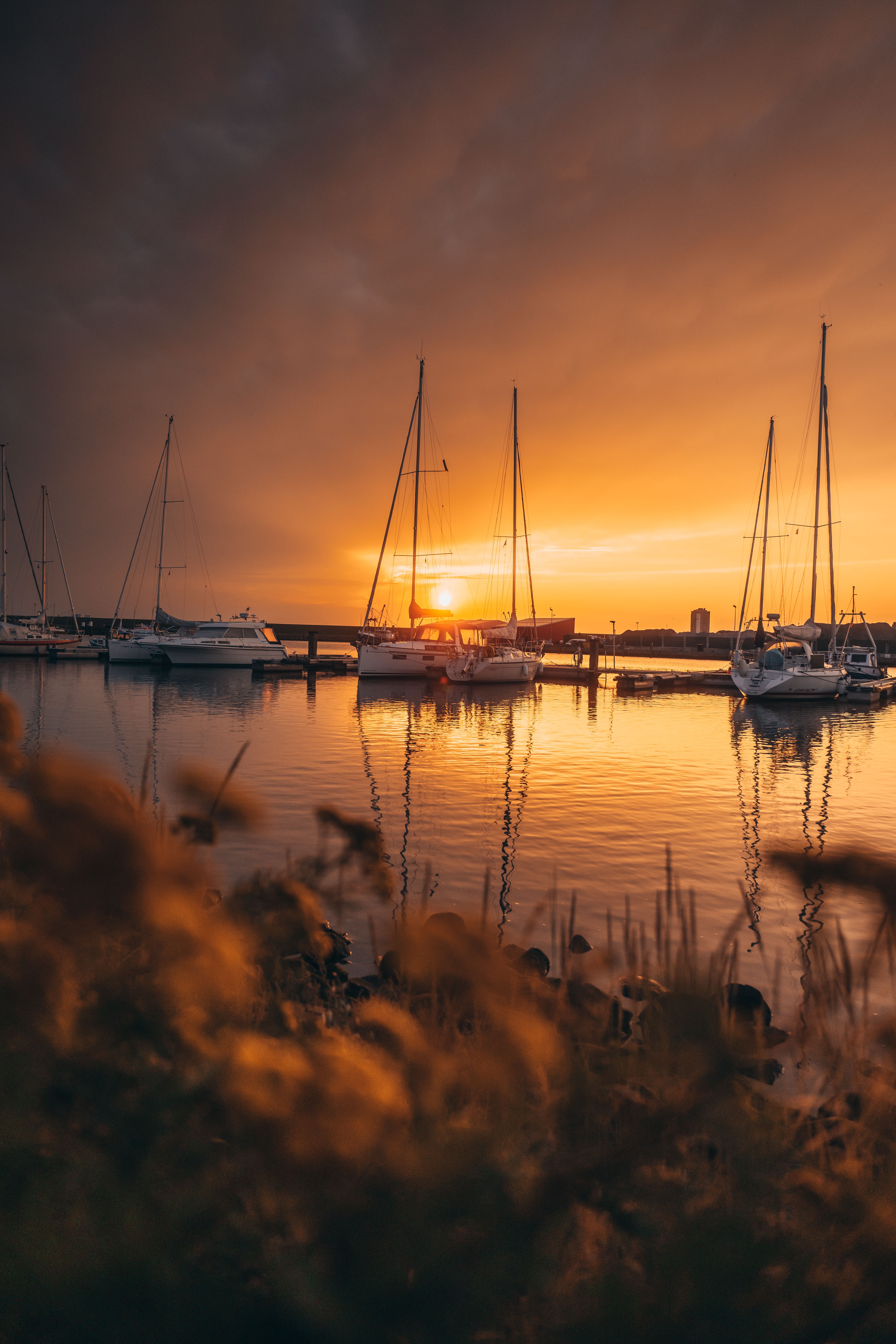 Die Sonne geht hinter kleinen Segelbooten im Büsumer Hafen unter, im Hintergrund steht das Büsumer Hochhaus