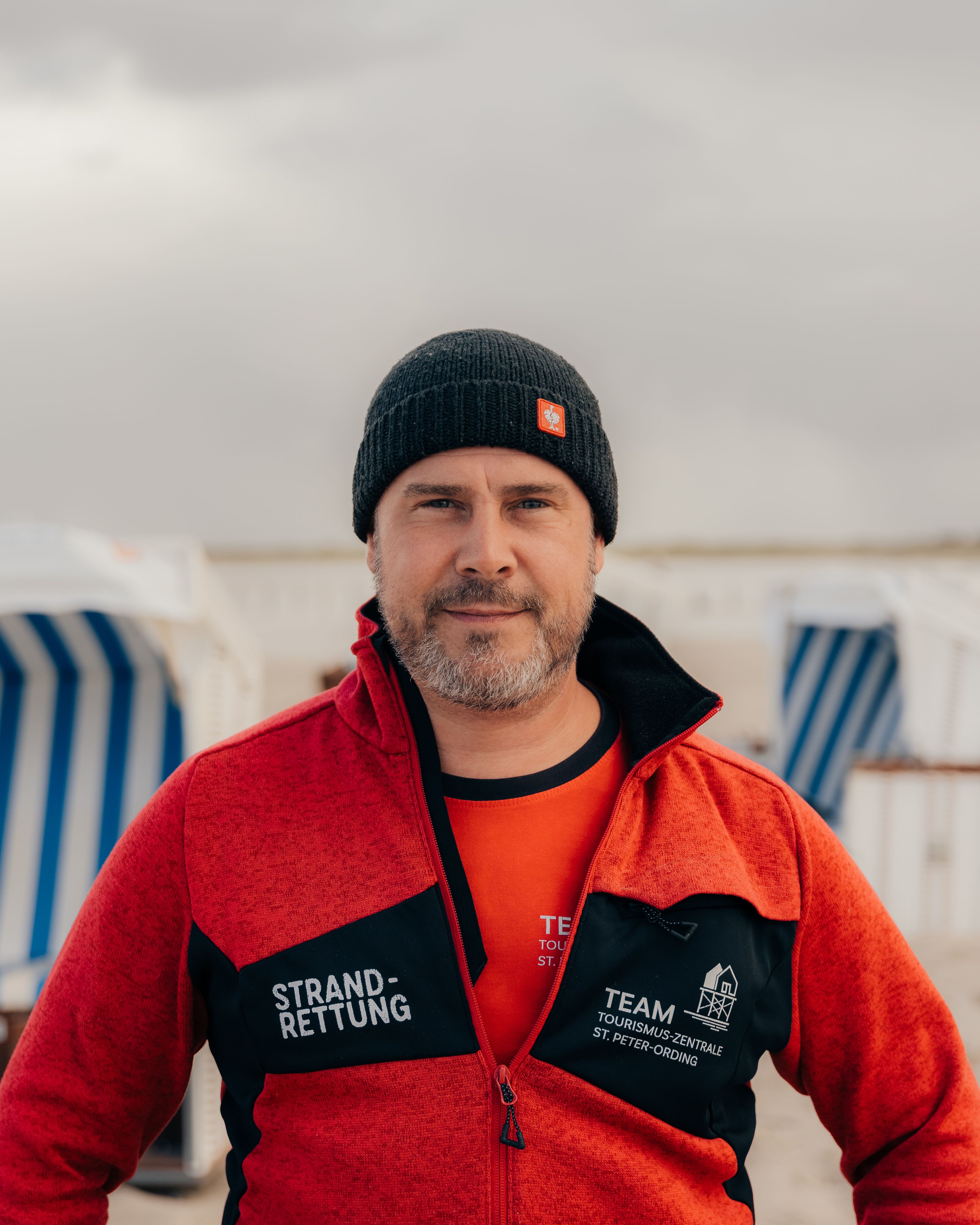 Ein Mitarbeiter der Strandrettung von St. Peter-Ording posiert vor einigen Strandkörben am Strand von St. Peter-Ording