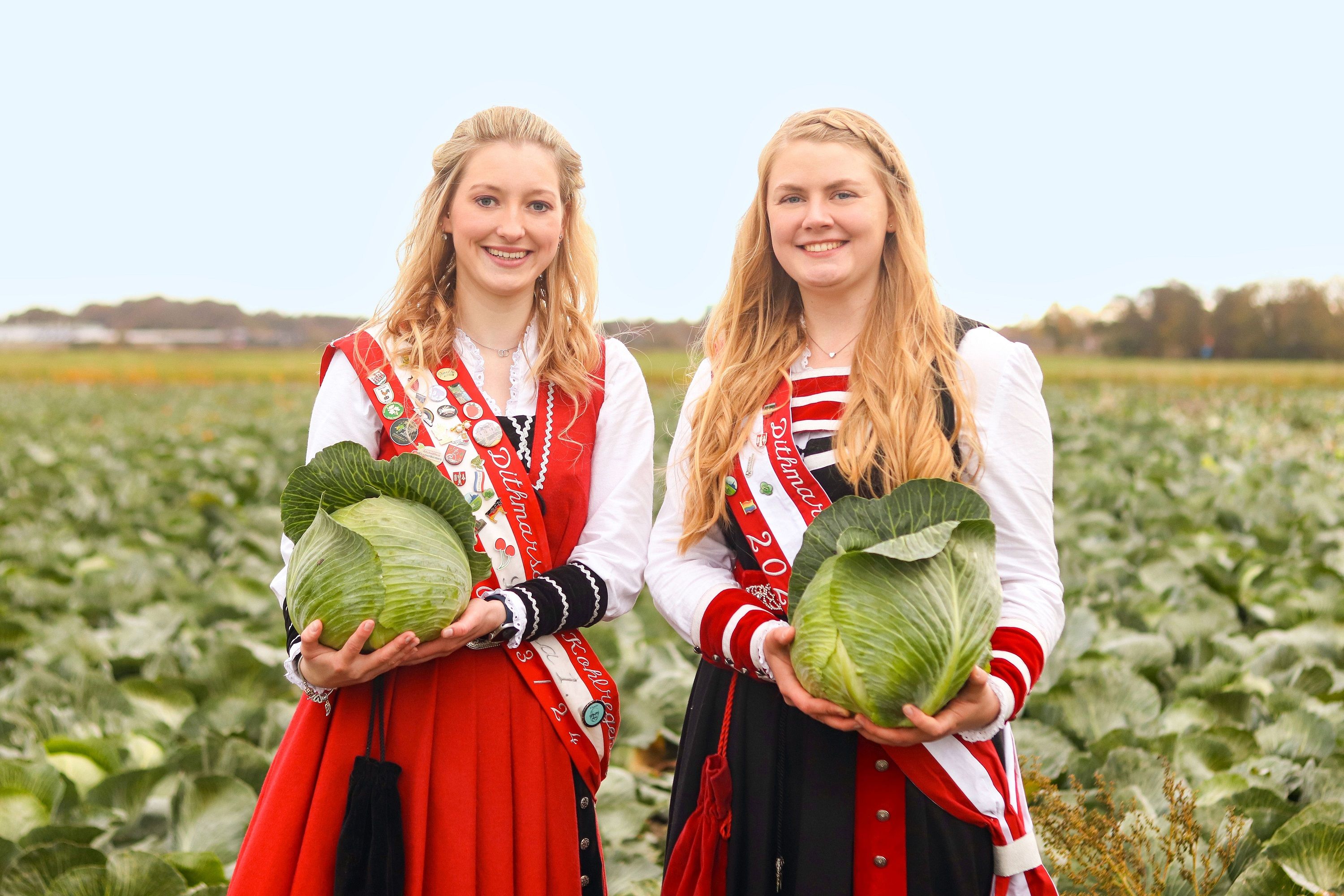 Die beiden amtierenden Kohlregentinnen von Dithmarschen vor einem Kohlfeld, gekleidet in der traditionellen Regentinnenkleidung