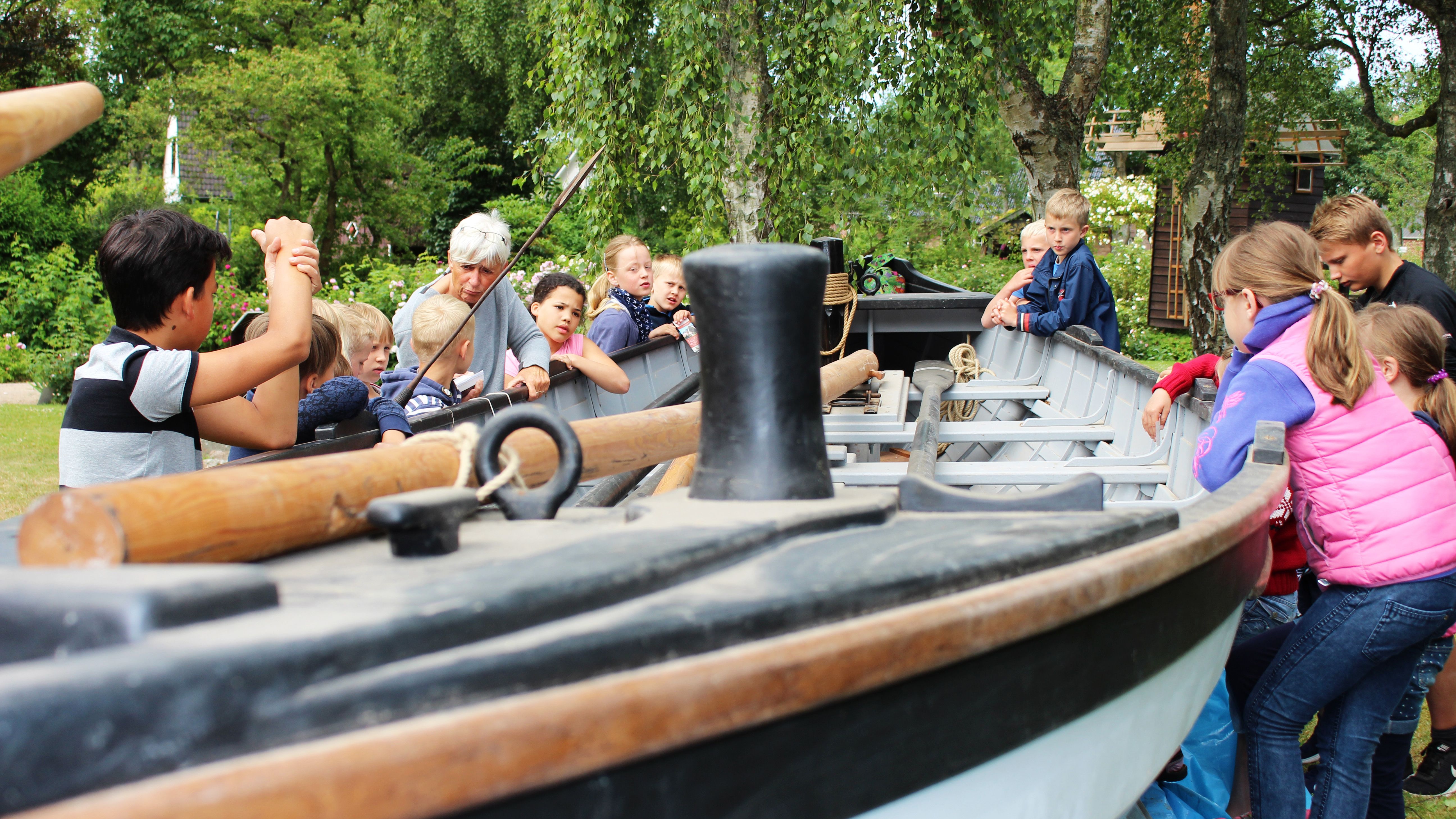 Kinder stehen um ein altes Boot herum und lauschen der "Dozentin" des Tages