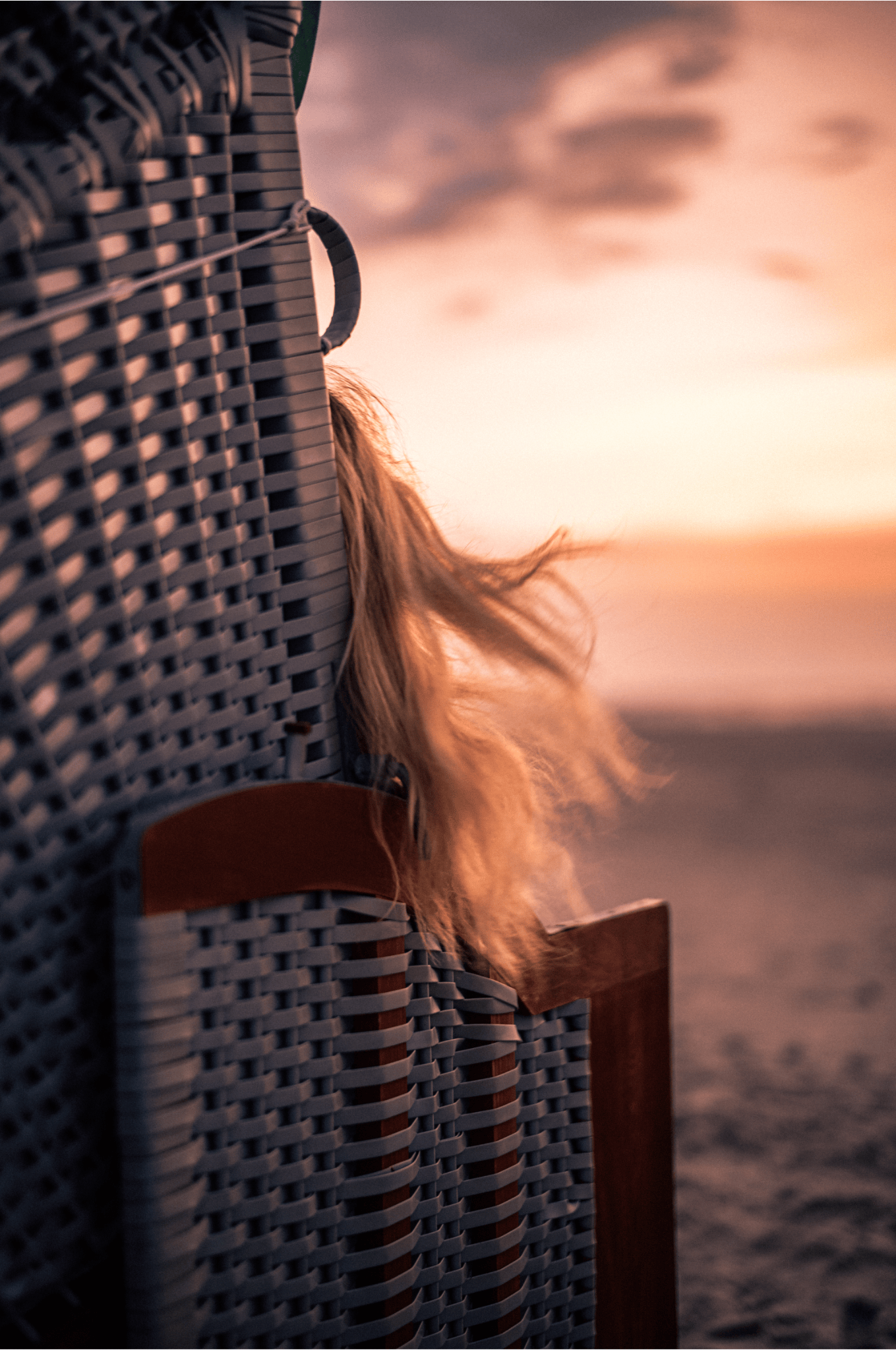 Lange Haare wehen aus einem Strandkorb auf Amrum hervor, während die Sonne untergeht.