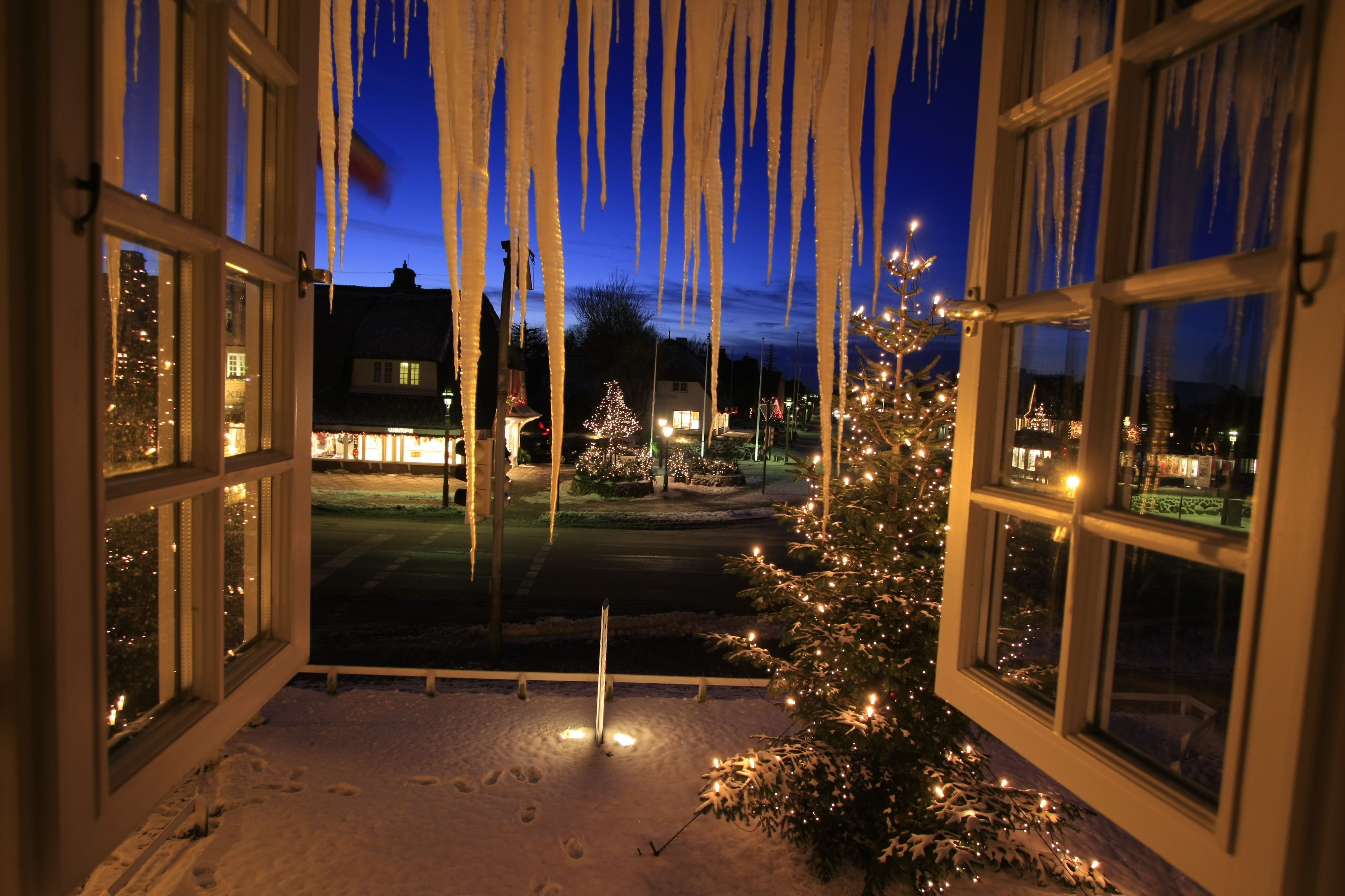 Blick aus einem Fenster auf den weihnachtlich geschmückten Platz mit zwei Weihnachtsbäumen